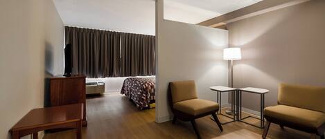 Habitación de hotel con una cama, dos sillones, una mesita, un escritorio, una lámpara y un televisor.
