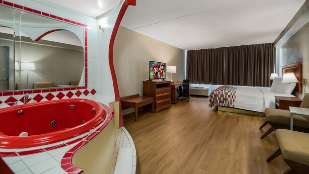 A hotel room with a red jacuzzi, a bed, a desk with a lamp, and a TV. - Red Roof Inn & Suites Newark - University (Newark)