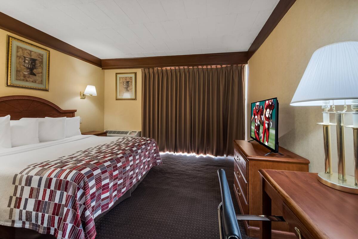 A hotel room with a large bed, a desk with a lamp, a television, and a window with curtains.