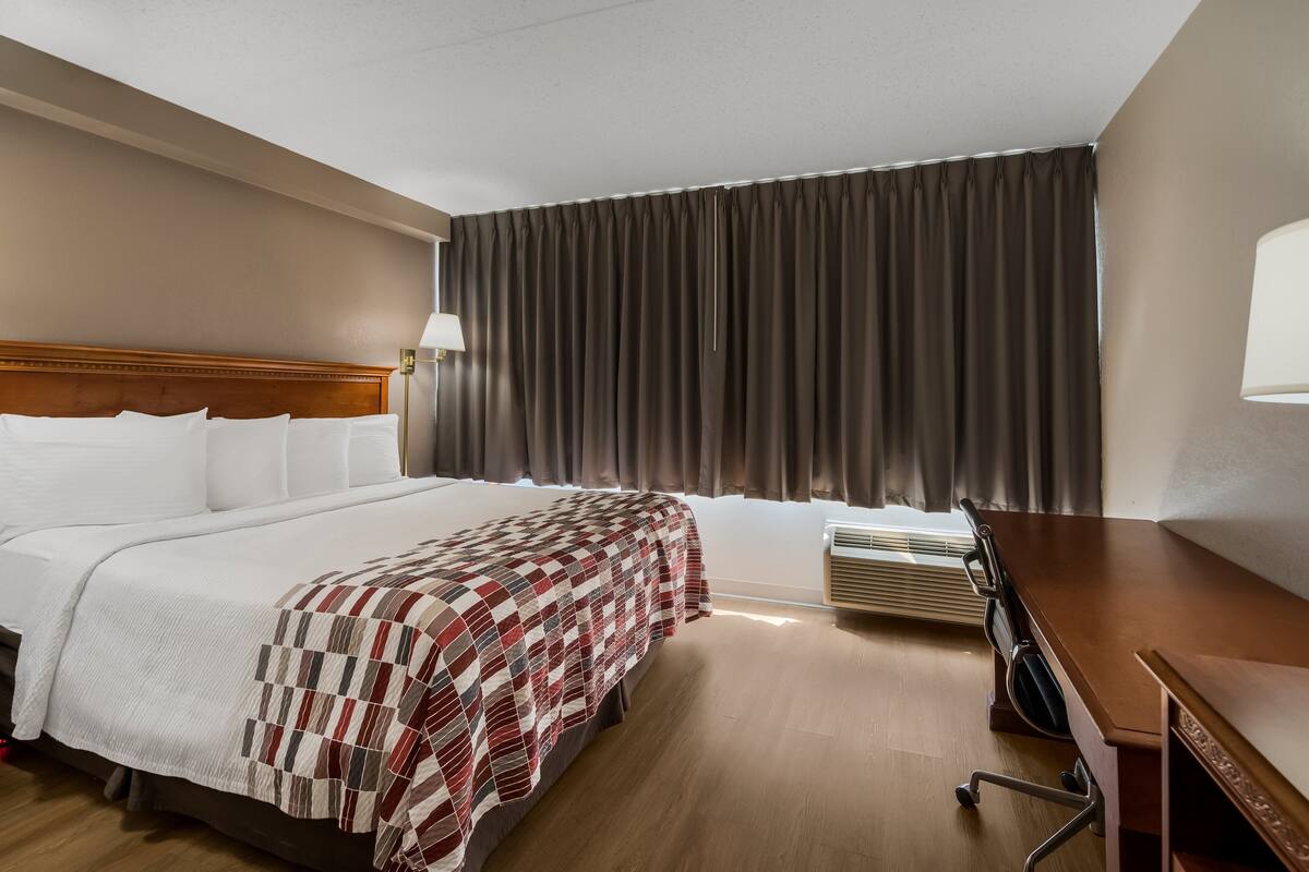 A hotel room with a large bed, a desk, a chair, a lamp, and a window with curtains.