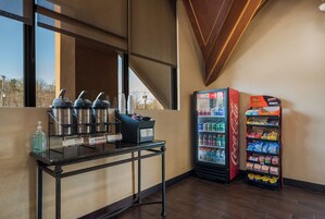 Una estación de bebidas de autoservicio con dispensadores, un refrigerador de Coca-Cola repleto de diversas bebidas y una máquina expendedora con aperitivos.