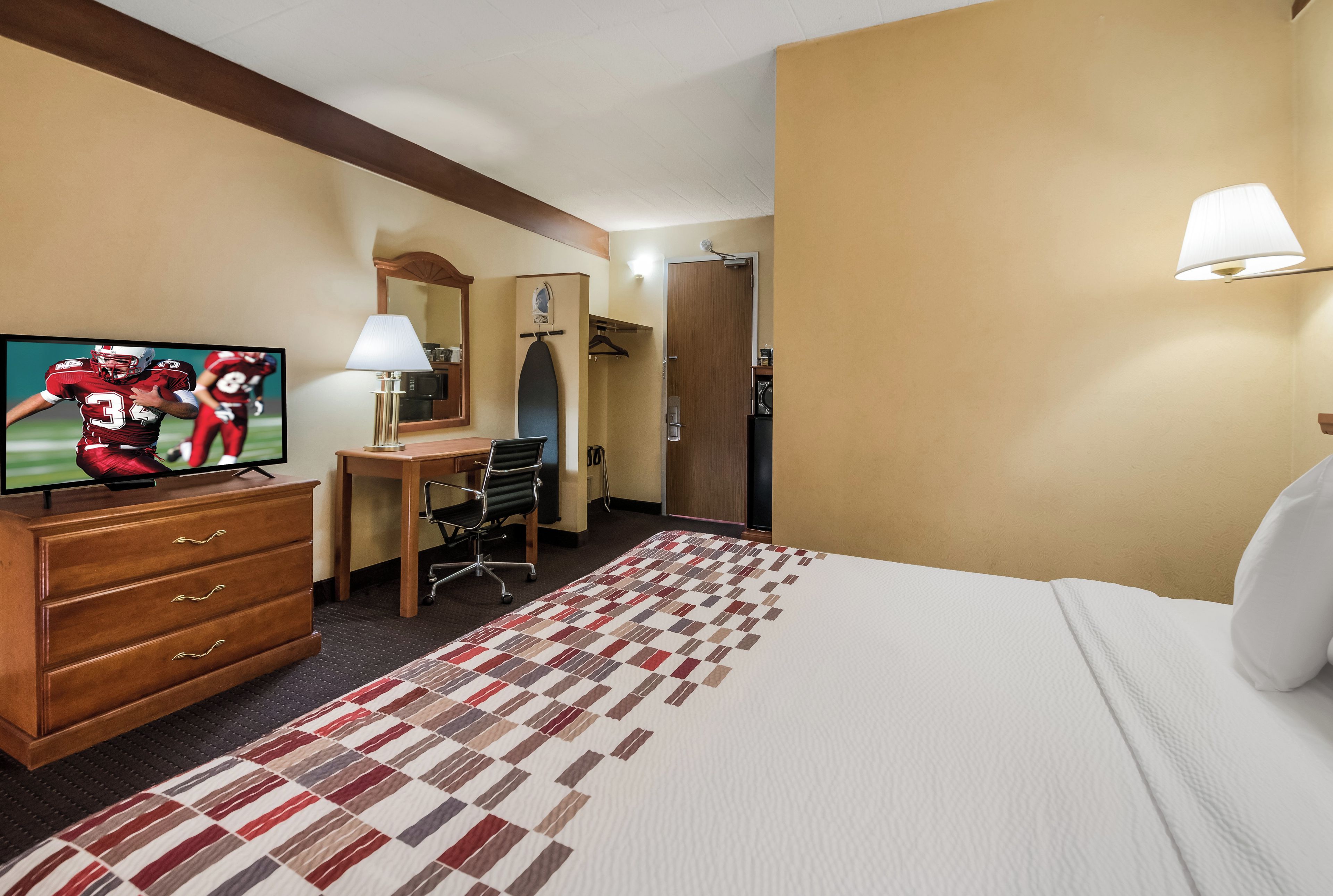 A hotel room with a bed, a desk, a television, a lamp, and a wardrobe.