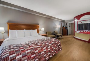 A hotel room with a large bed, a desk, two chairs, a mirror, and a bathroom visible through an archway. - Red Roof Inn & Suites Newark - University (Newark)