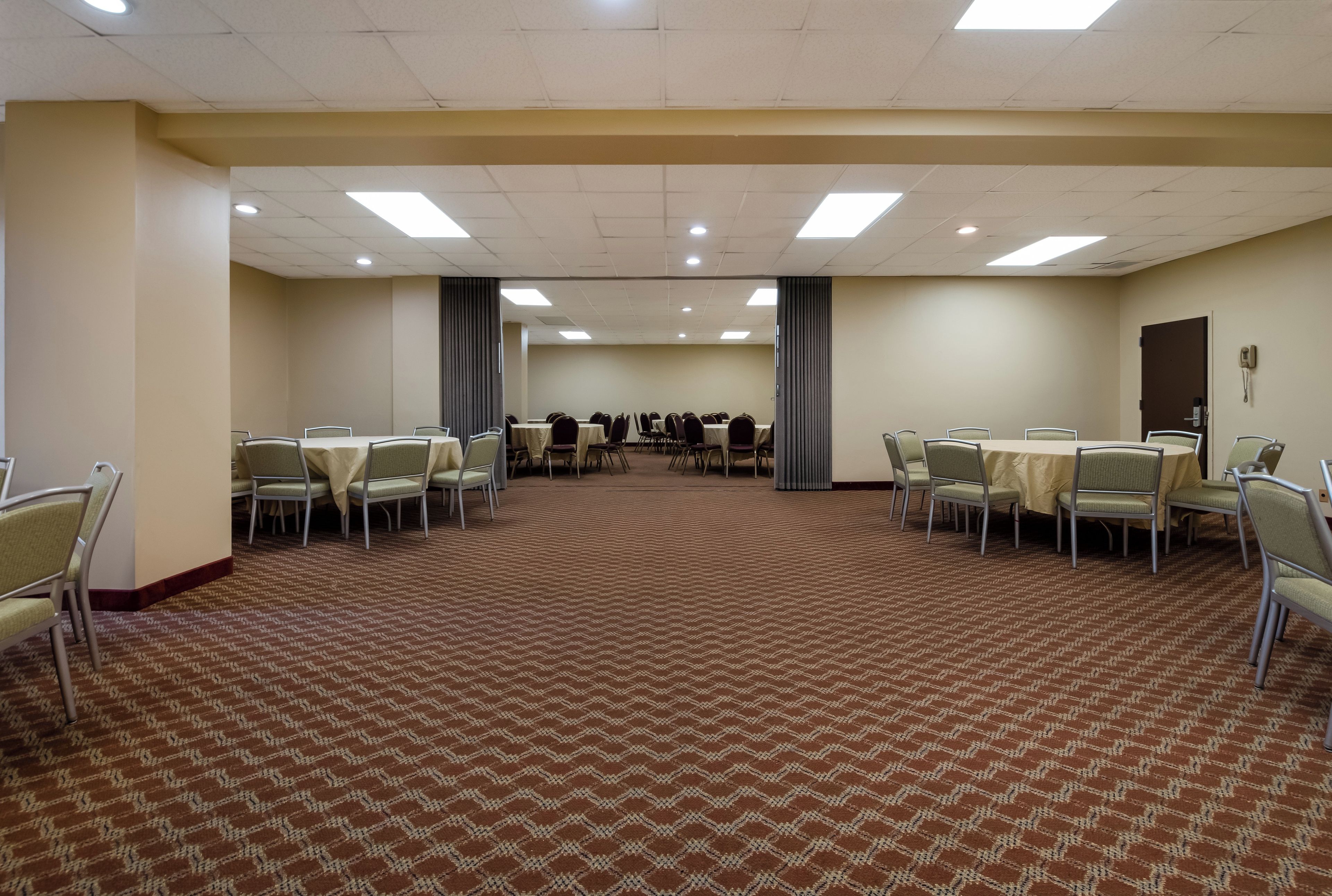 A conference room with tables and chairs, carpeted floor, and a plain wall with a door.