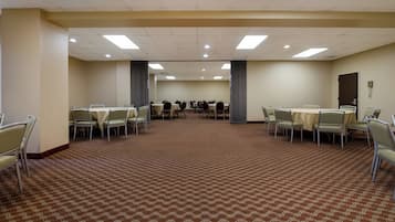 A conference room with tables and chairs, carpeted floor, and a plain wall with a door.