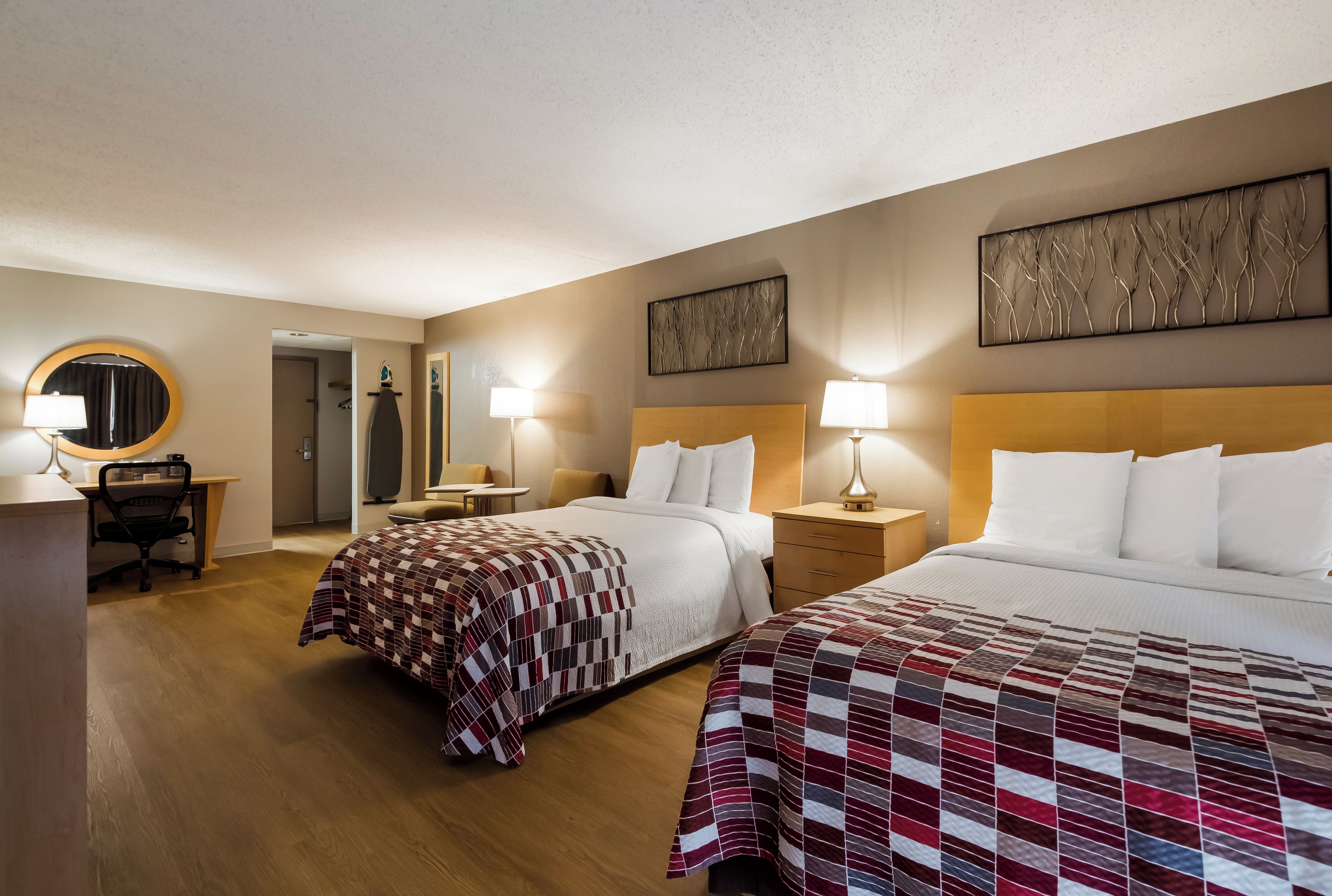 A hotel room with two beds, a desk, a chair, and a mirror.