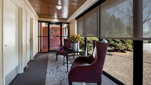 A covered corridor with a wooden ceiling, a glass door leading outside, a table with chairs, and a potted plant. - Red Roof Inn & Suites Newark - University (Newark)