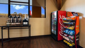 A corner of a hotel room with a table holding kettles and cups, a refrigerator stocked with snacks, and a window offering a view of trees and a clear sky. - Red Roof Inn & Suites Newark - University (Newark)