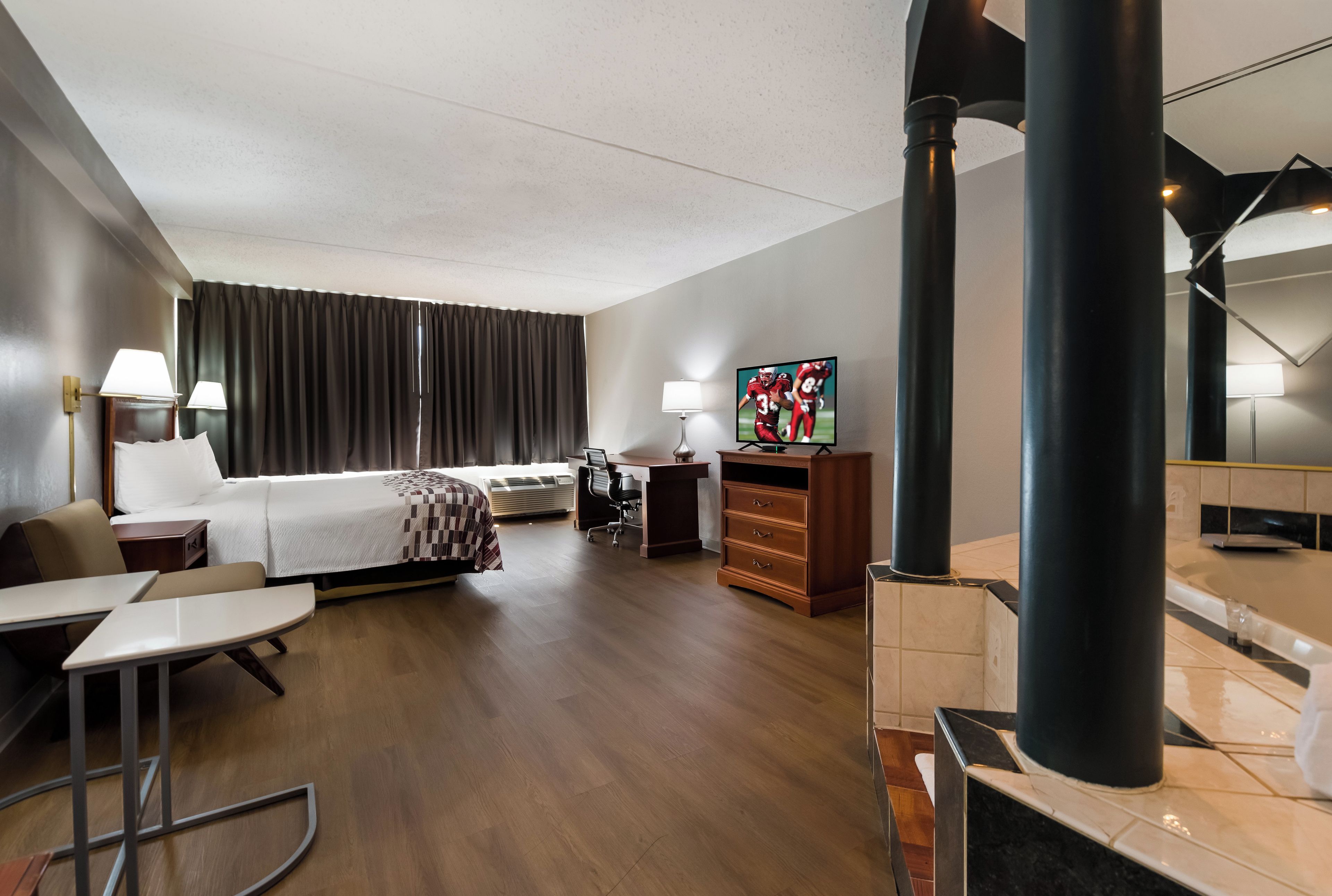 Une chambre d’hôtel comprenant un lit, un bureau, une chaise, une télévision et une salle de bain avec baignoire.