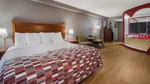 A hotel room with a large bed, a desk, two chairs, a mirror, and a bathroom visible through an archway. - Red Roof Inn & Suites Newark - University (Newark)
