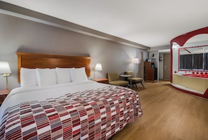 A hotel room with a large bed, a desk, two chairs, a mirror, and a bathroom visible through an archway. - Red Roof Inn & Suites Newark - University (Newark)