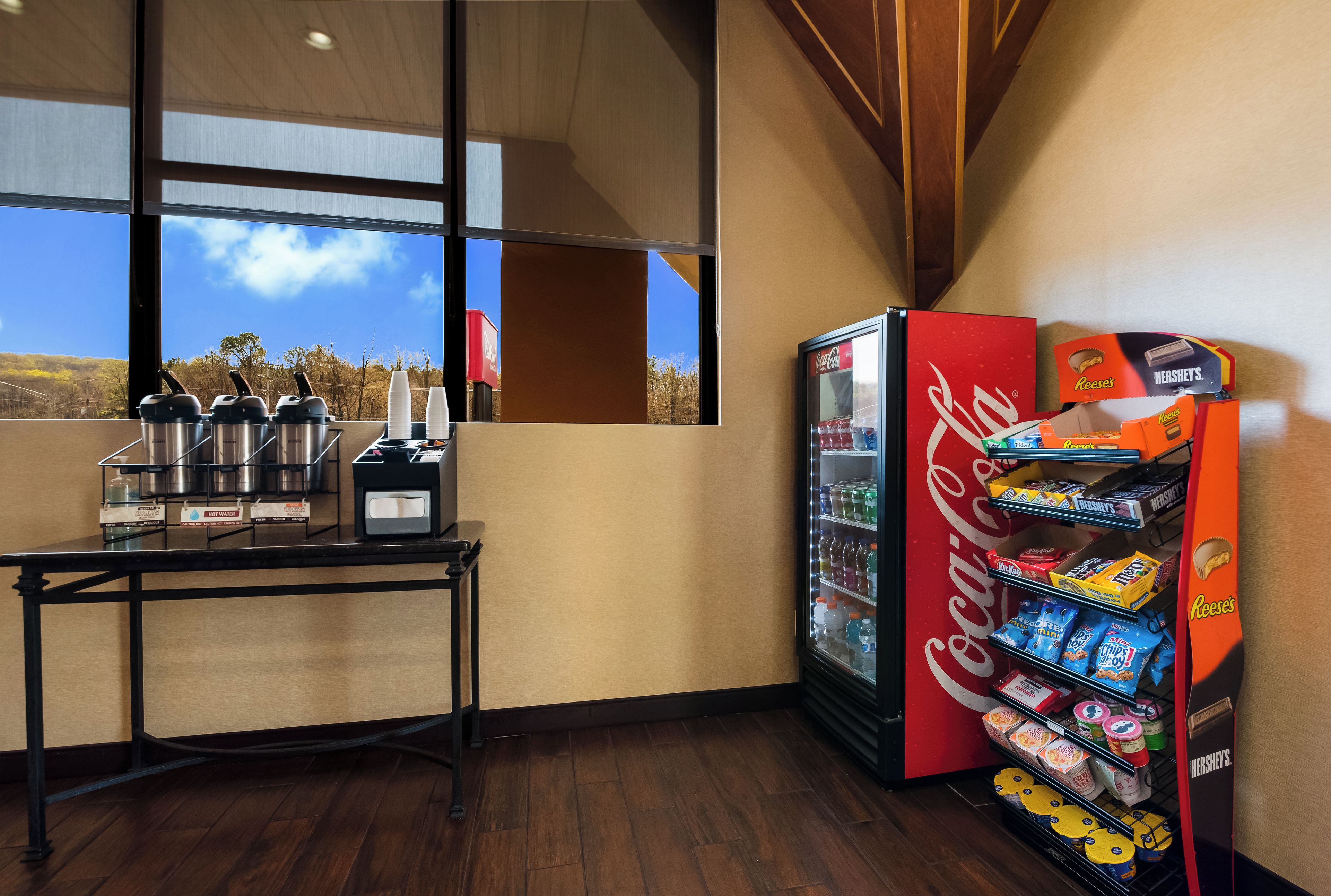 A corner of a room with a coffee station, a refrigerator stocked with beverages, and a vending machine with snacks.