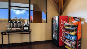 A corner of a room with a coffee station, a refrigerator stocked with beverages, and a vending machine with snacks.
