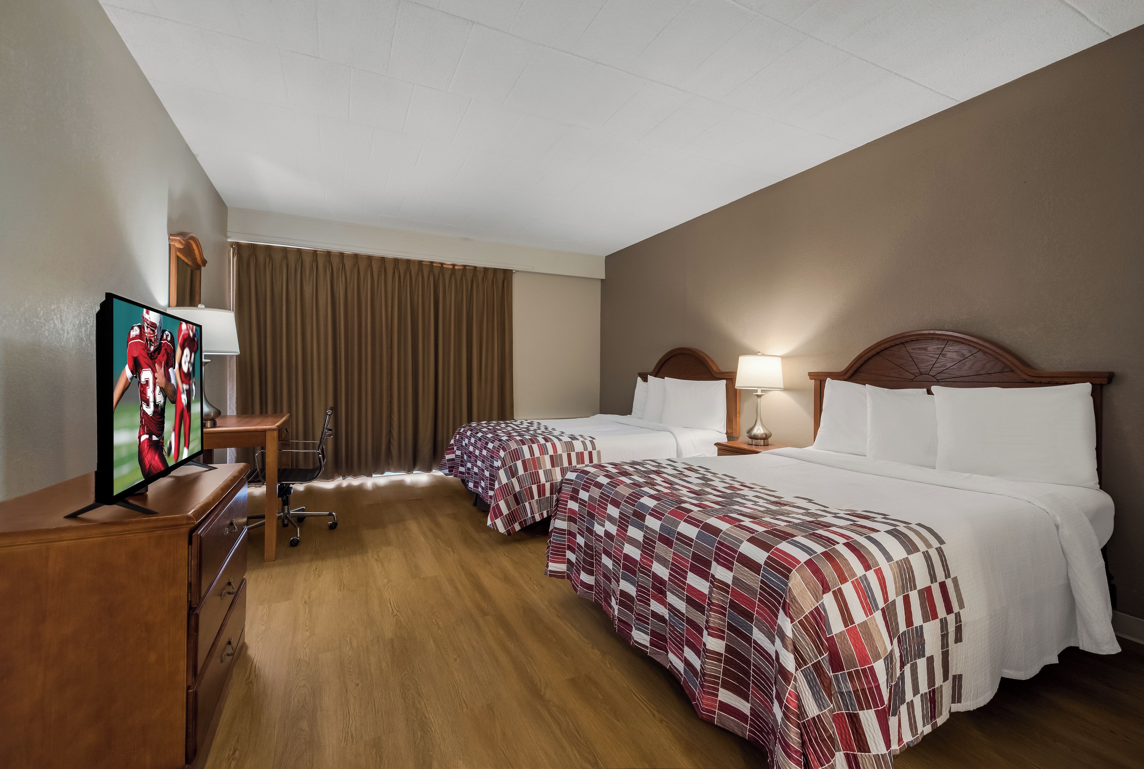 Habitación de hotel con dos camas, un escritorio, un televisor y una silla.