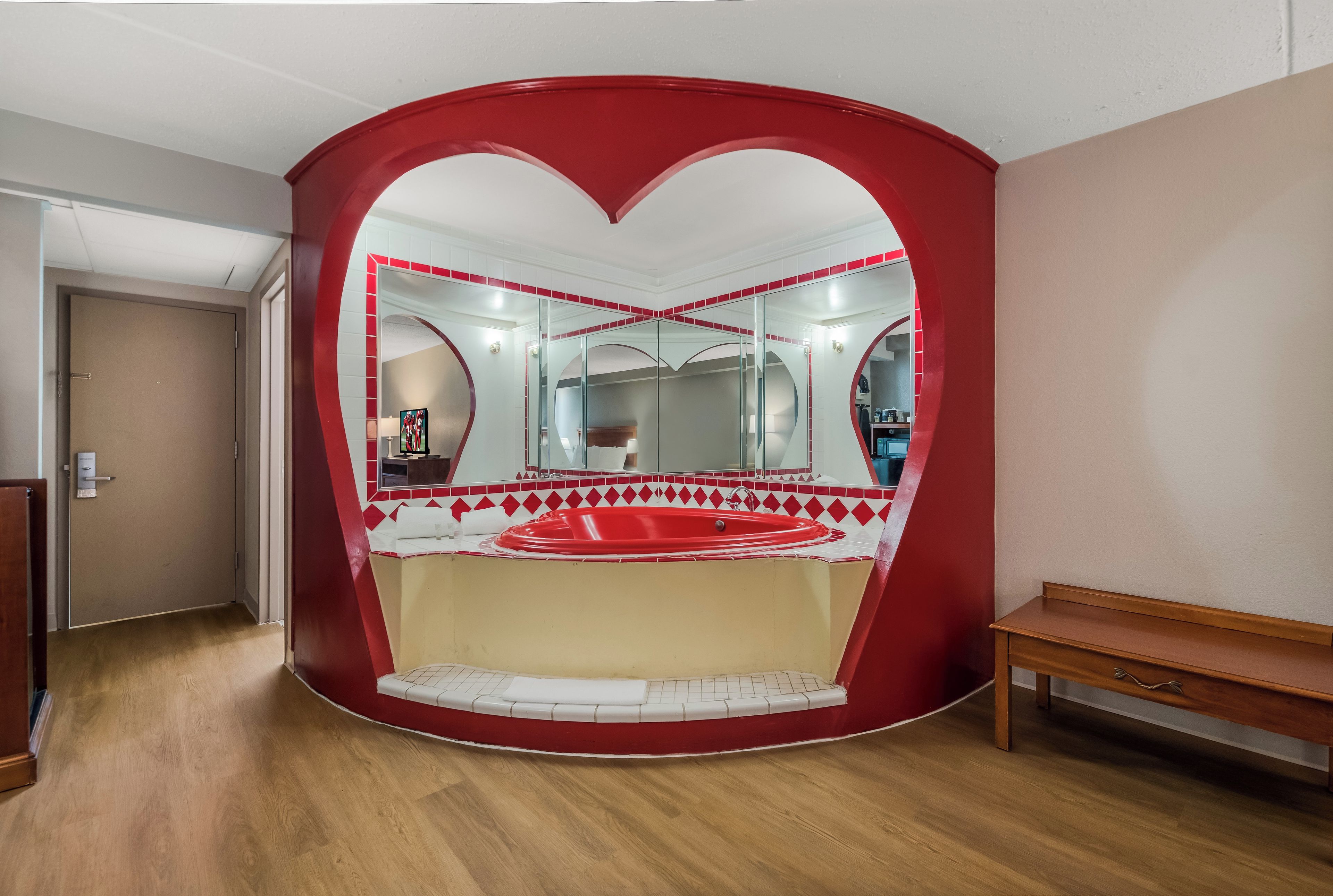 Une pièce dont le mur est décoré d’un motif en forme de cœur, et qui contient un lit, un banc et un miroir.