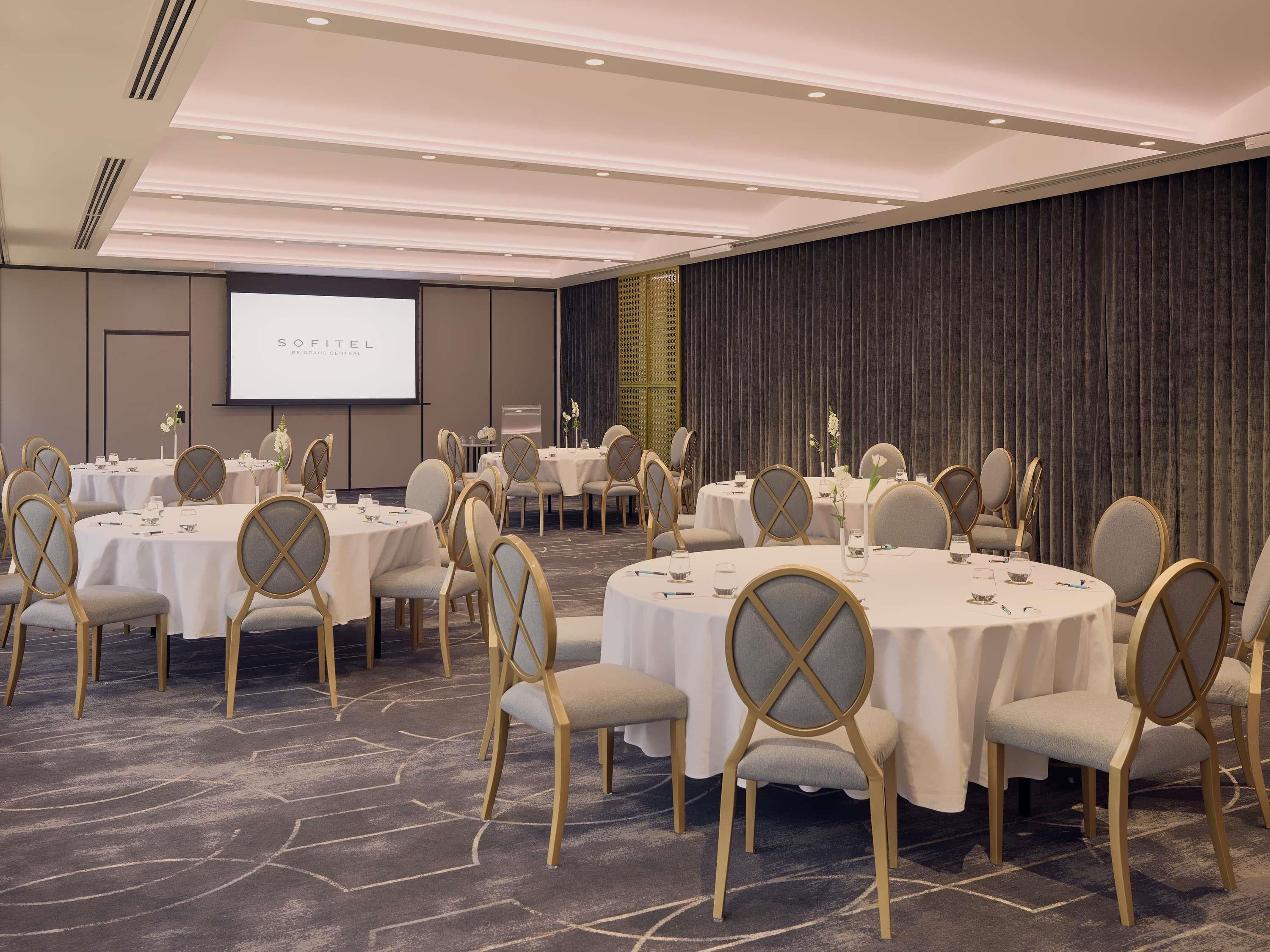 A conference room with round tables, chairs, and a projector screen.