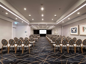 A conference room with rows of chairs, a projector screen, and framed artwork on the walls. - Sofitel Brisbane Central (Brisbane)