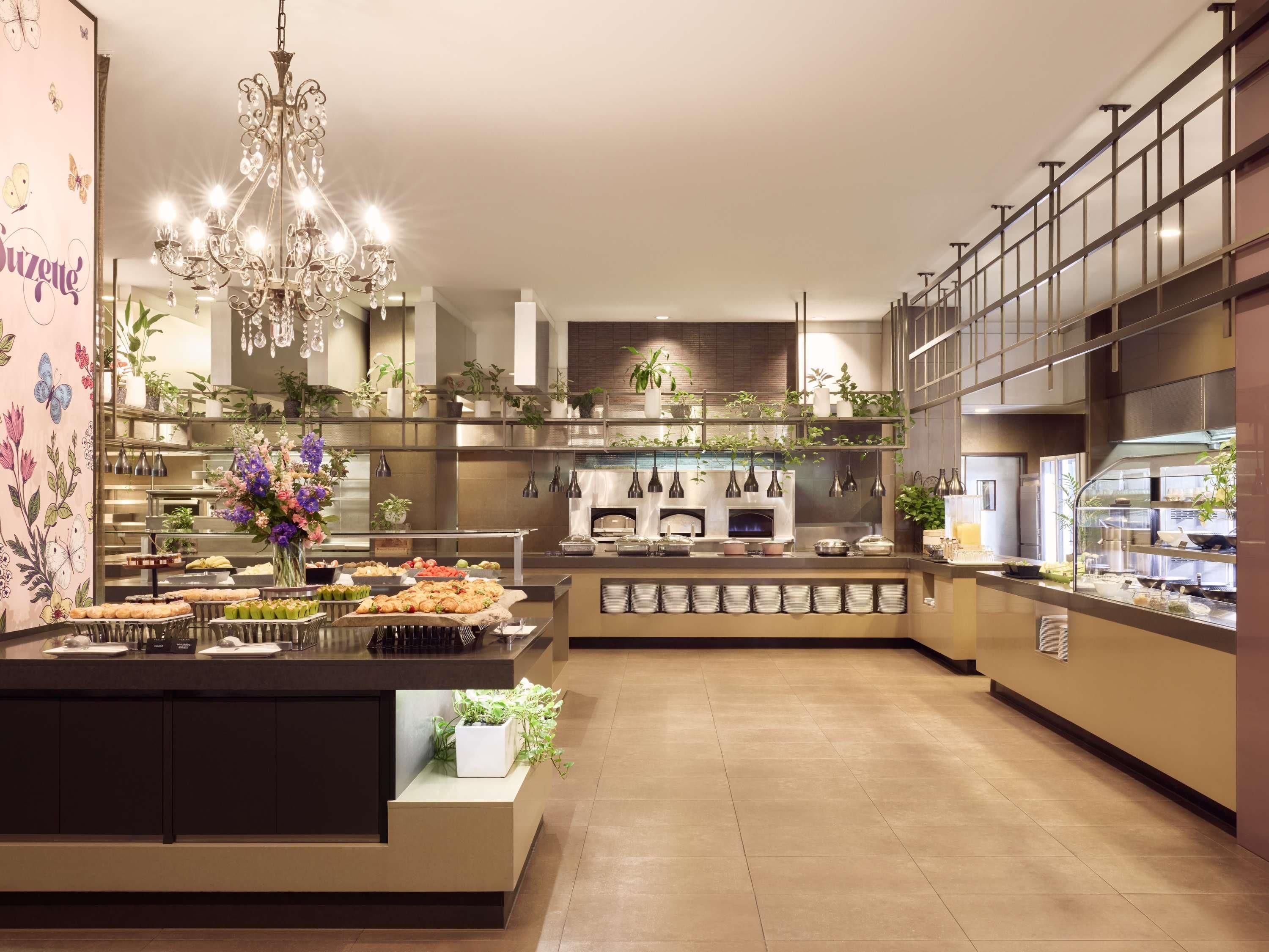 Une cuisine moderne dotée d’un îlot central, de nombreuses étagères ornées de plantes et d’un lustre.