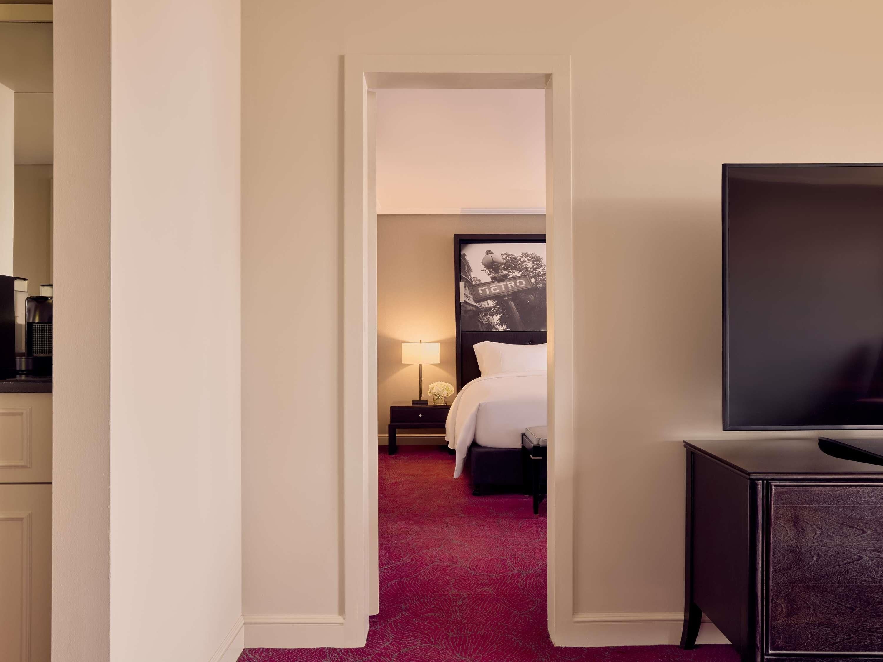 A hotel room with a bed, a TV, a nightstand, and a wall-mounted picture.