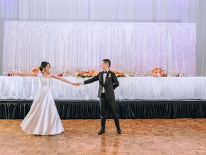 A couple dancing in a room with a wooden floor, a white table with floral centerpieces, and a backdrop of sheer curtains with string lights. - Sofitel Brisbane Central (Brisbane)