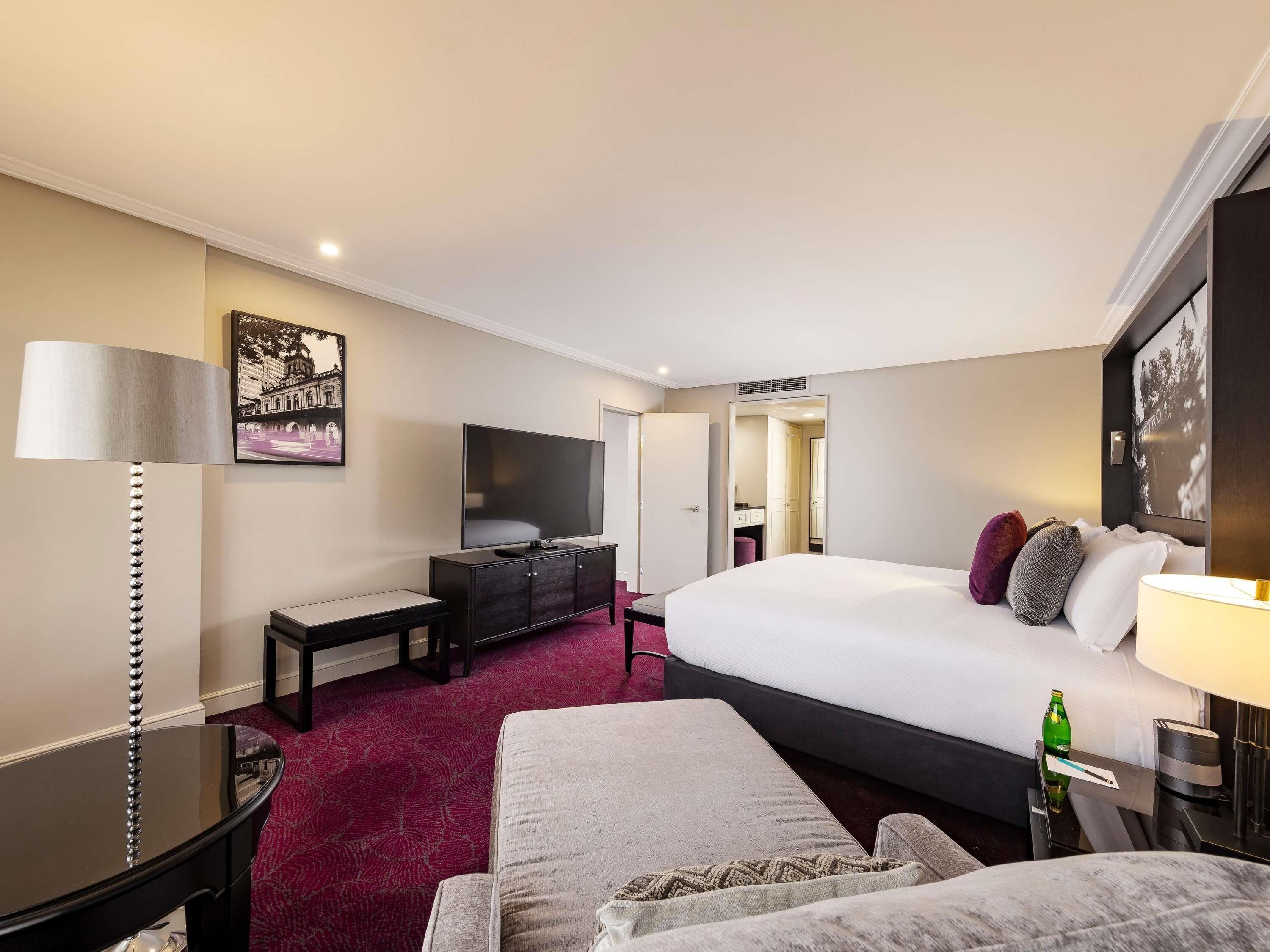 A hotel room with a bed, a desk, a chair, a TV, and a mirror.