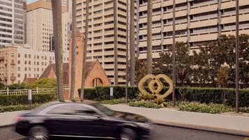 A modern urban street with high-rise buildings, a moving car, and a distinctive golden sculpture in the foreground.