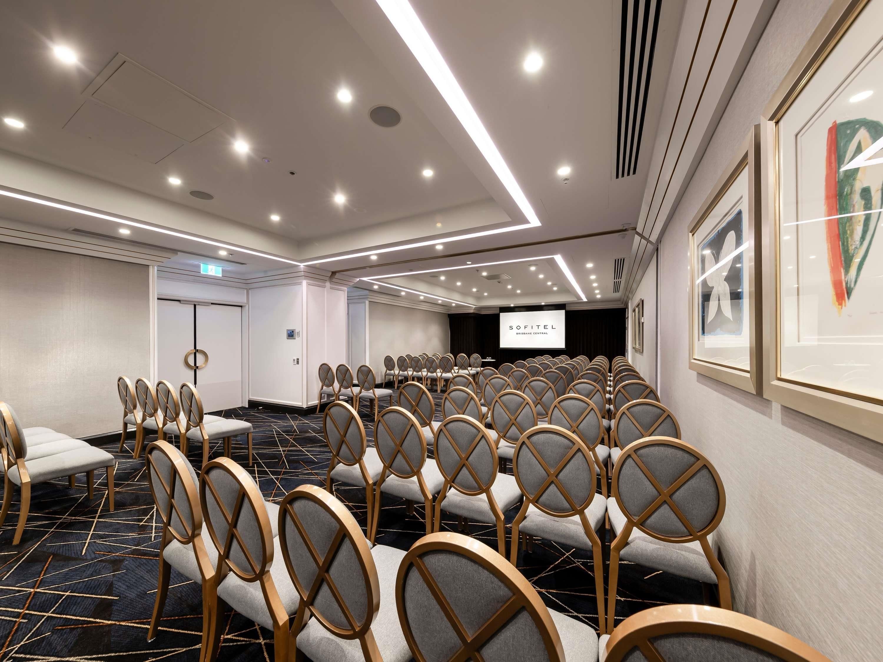 A conference room with rows of chairs, a projector screen, and framed artwork on the walls.