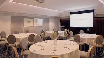 A conference room with round tables, chairs, and a projection screen displaying 'SOFITEL BRISBANE CENTRAL'.