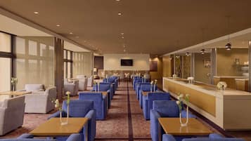 A hotel lobby with rows of seating, a reception desk, and large windows.