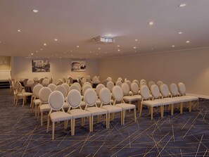 A conference room with rows of chairs, tables, a projector, and a cityscape painting on the wall. - Sofitel Brisbane Central (Brisbane)