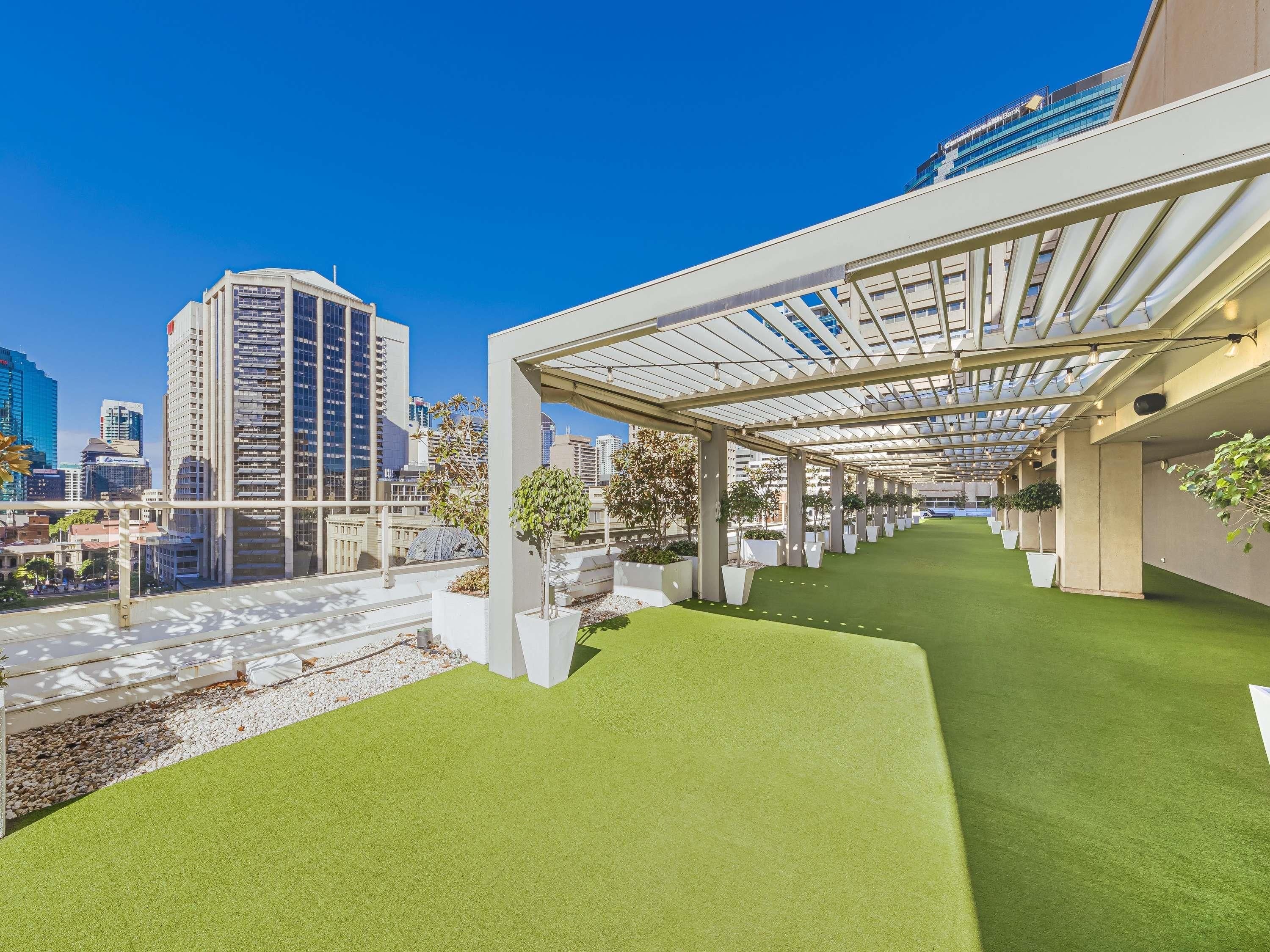 A rooftop terrace with artificial grass, potted plants, and a view of city buildings.