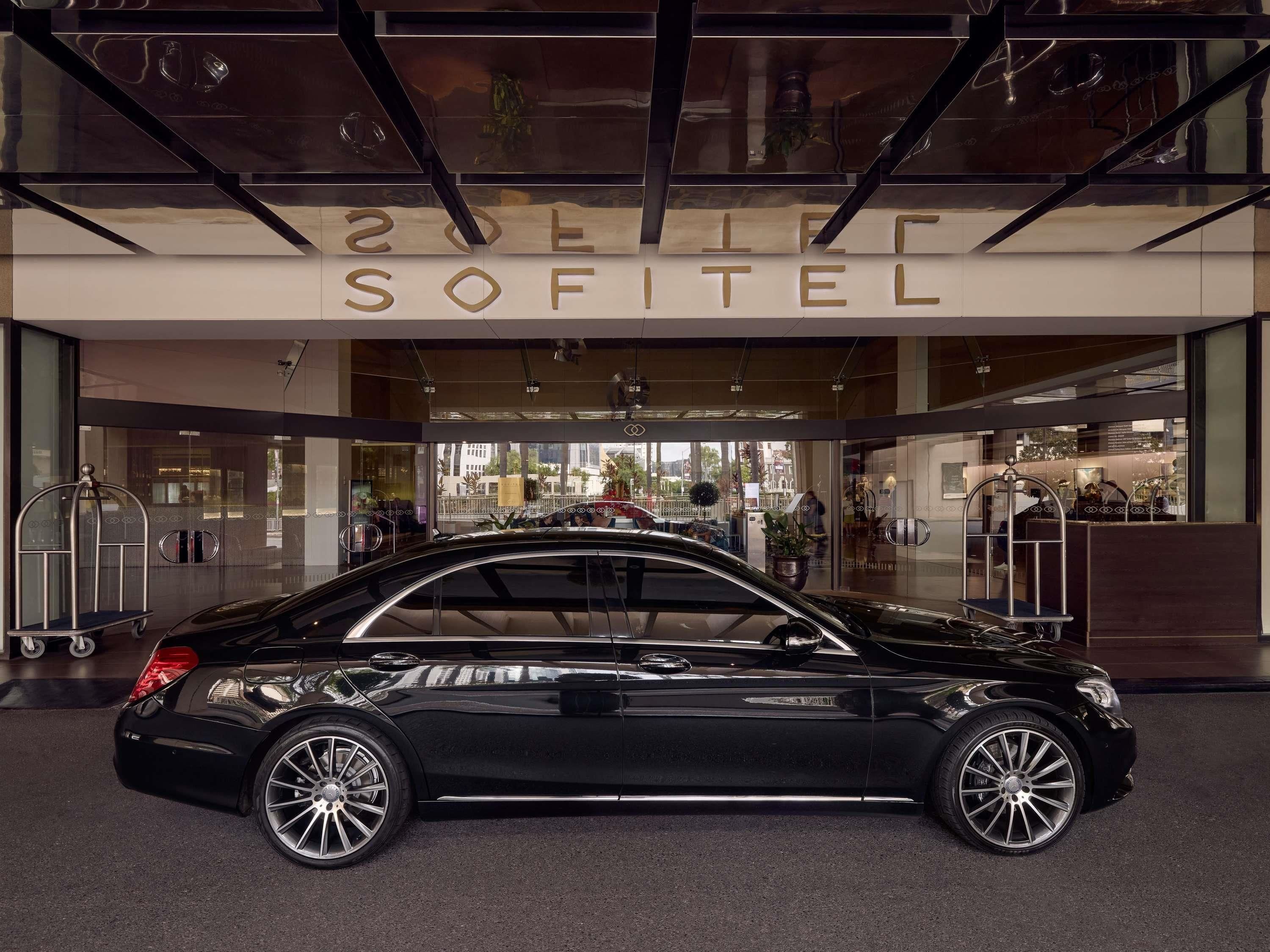 Un cotxe negre estacionat davant de l'entrada d'un hotel on es pot veure el nom 'SOFITEL'.