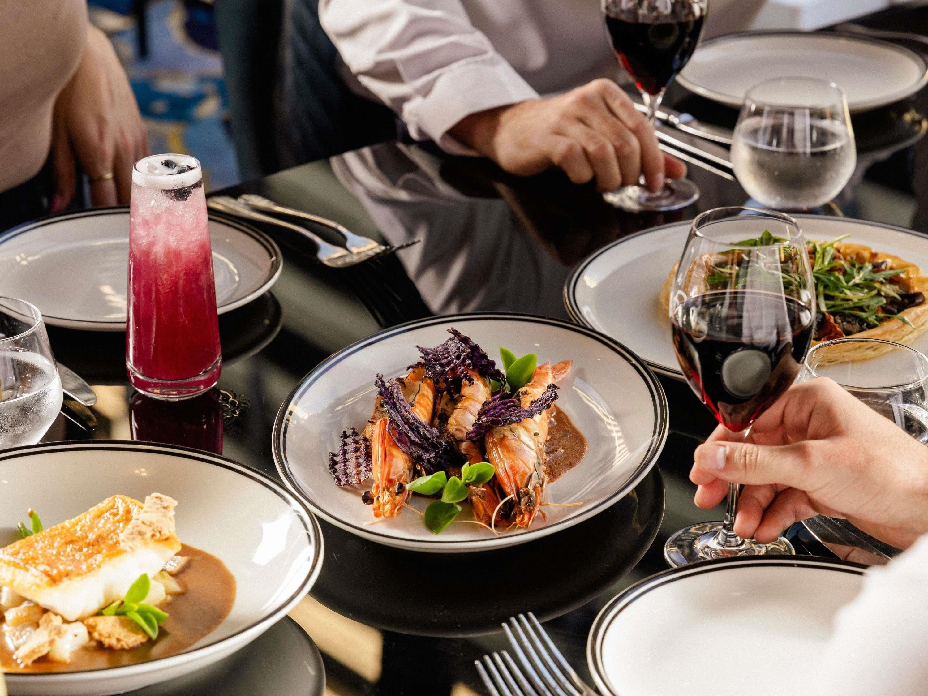 Een eettafel met borden eten, glazen rode wijn en een cocktail.
