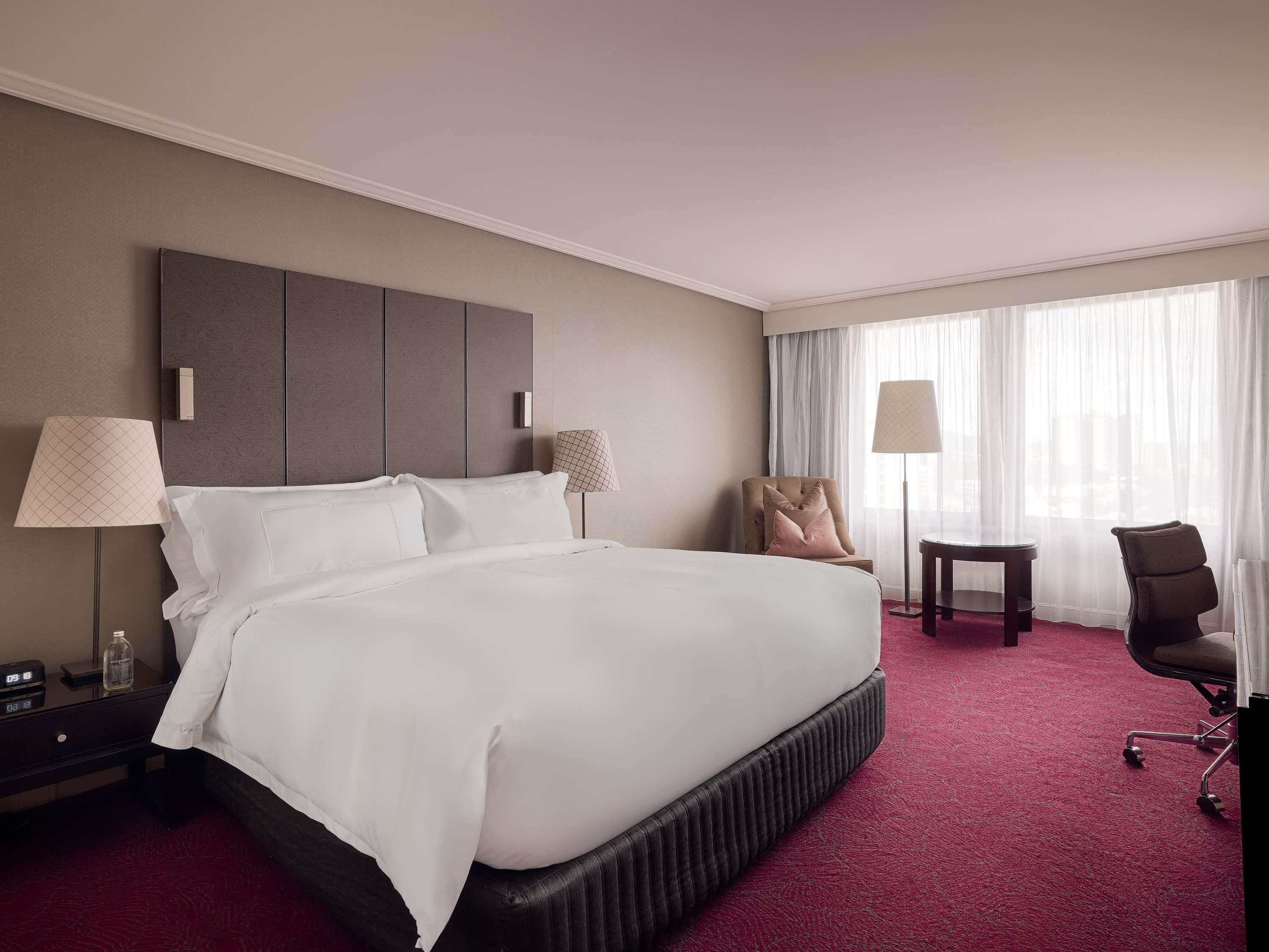 Ein Hotelzimmer mit einem großen Bett, Nachttischen, einem Schreibtisch und einem Sessel.
