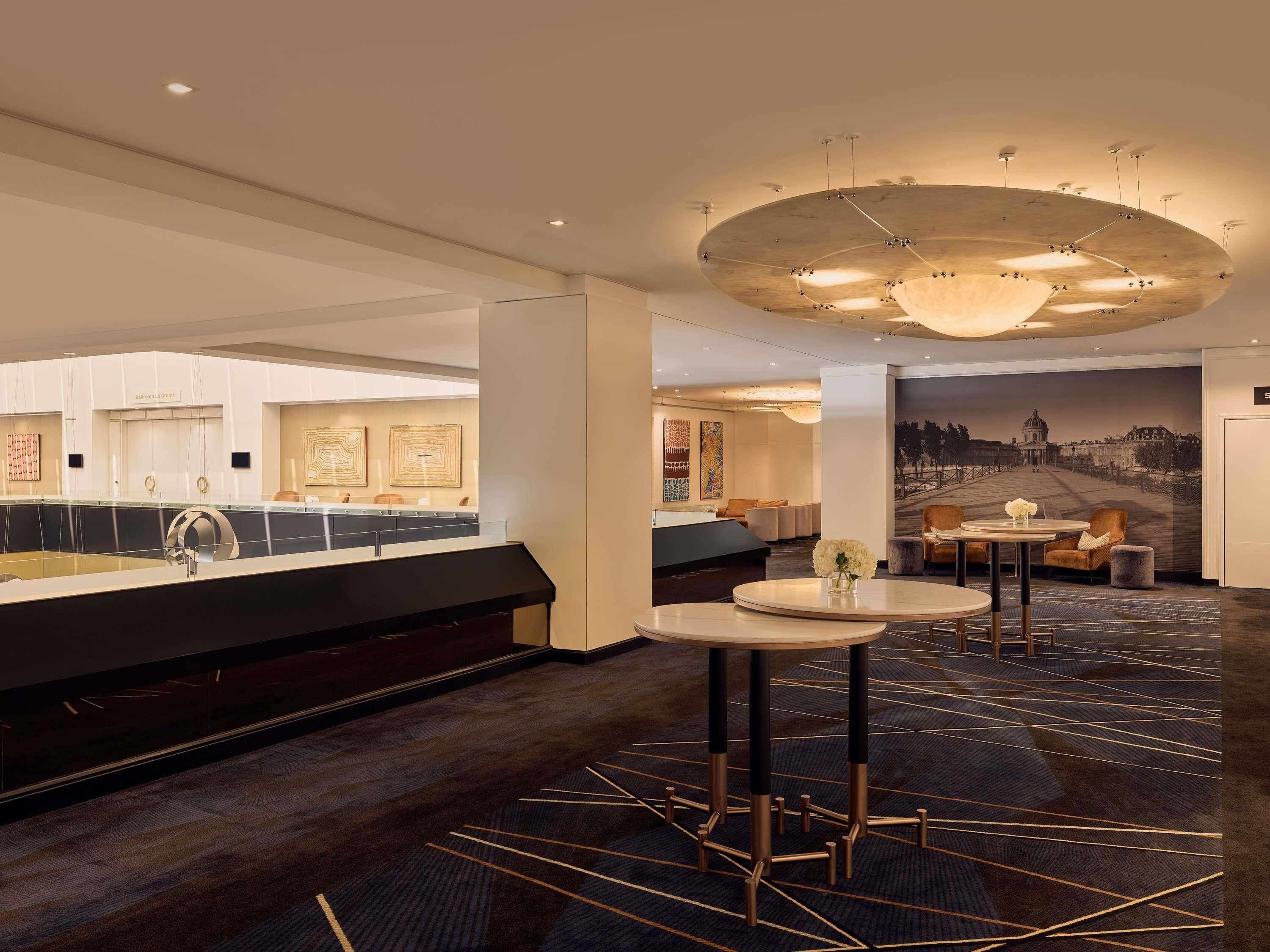 A modern hotel lobby with a reception desk, seating area, and a large mural.