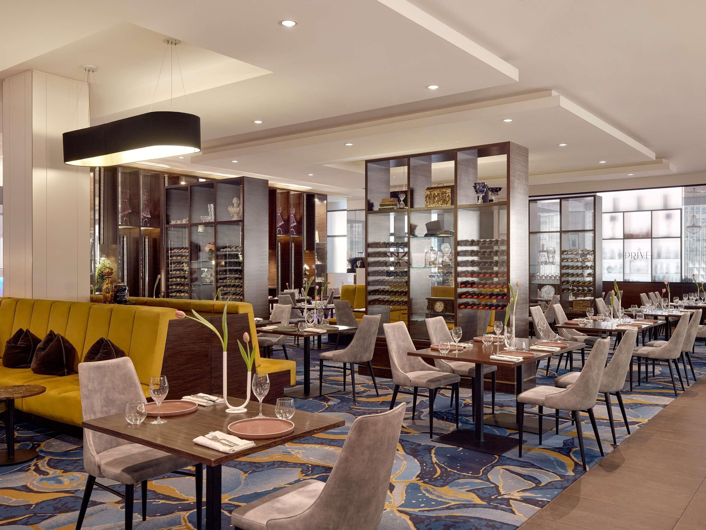 A hotel dining area with multiple tables, chairs, and a yellow sofa.