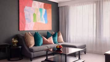 A modern living room with a grey sofa, colorful cushions, a glass coffee table, and a large abstract painting on the wall.