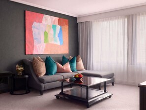 A modern living room with a grey sofa, colorful cushions, a glass coffee table, and a large abstract painting on the wall. - Sofitel Brisbane Central (Brisbane)