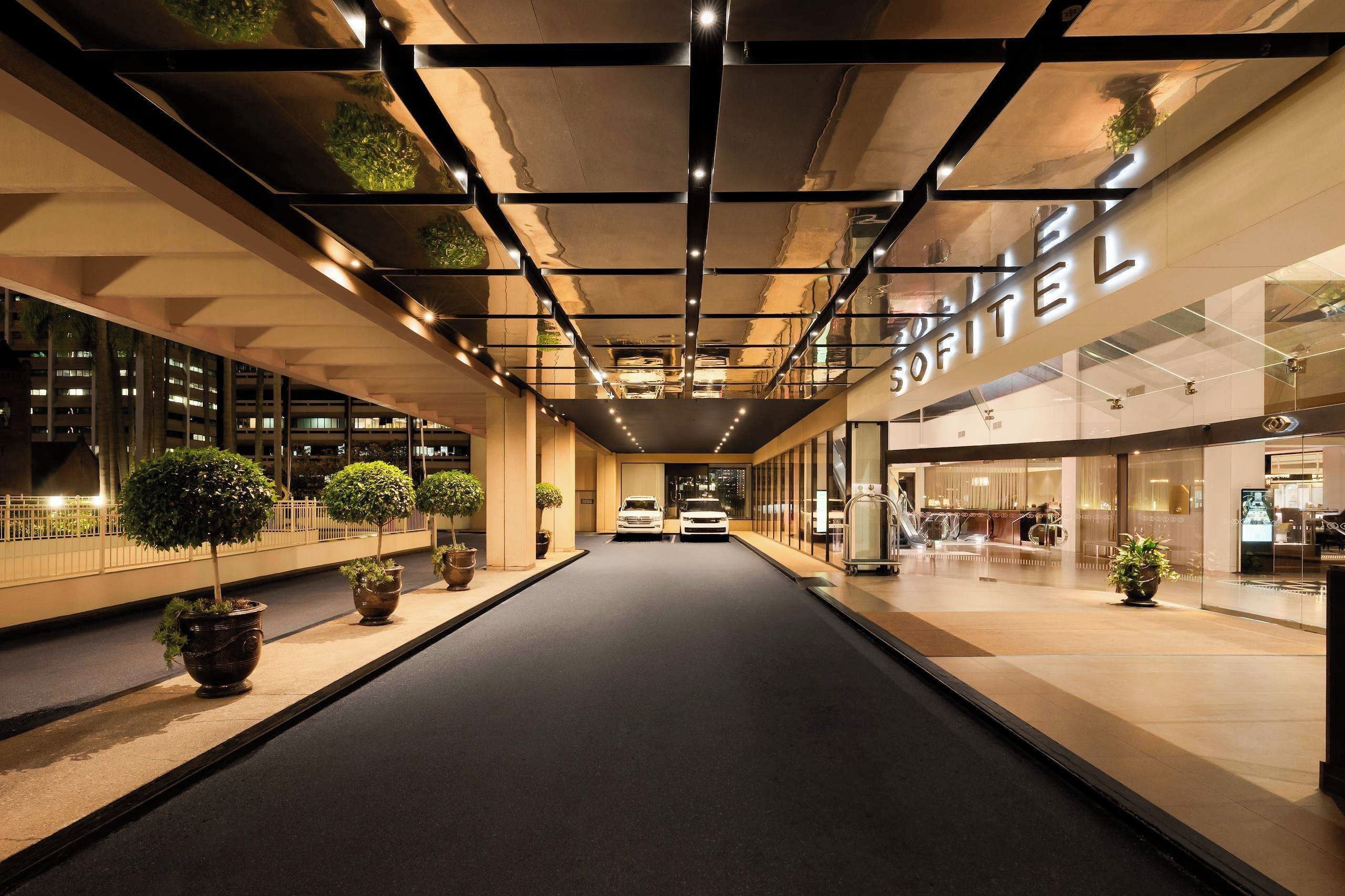 A modern hotel corridor with a central walkway, potted plants, and a car parked at the end.