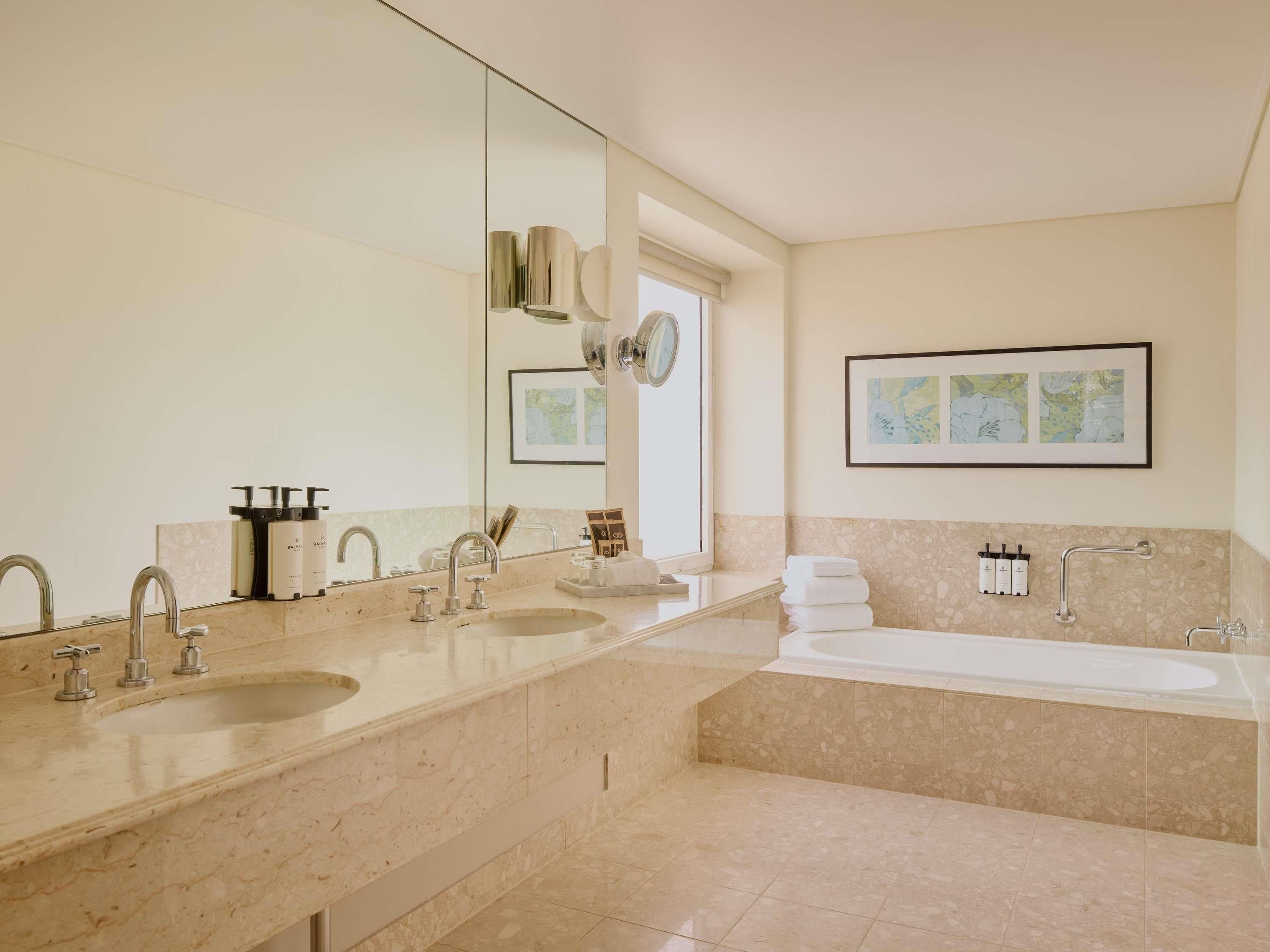 Une salle de bain moderne avec un grand miroir, deux lavabos, une baignoire et une œuvre d’art encadrée accrochée au mur.