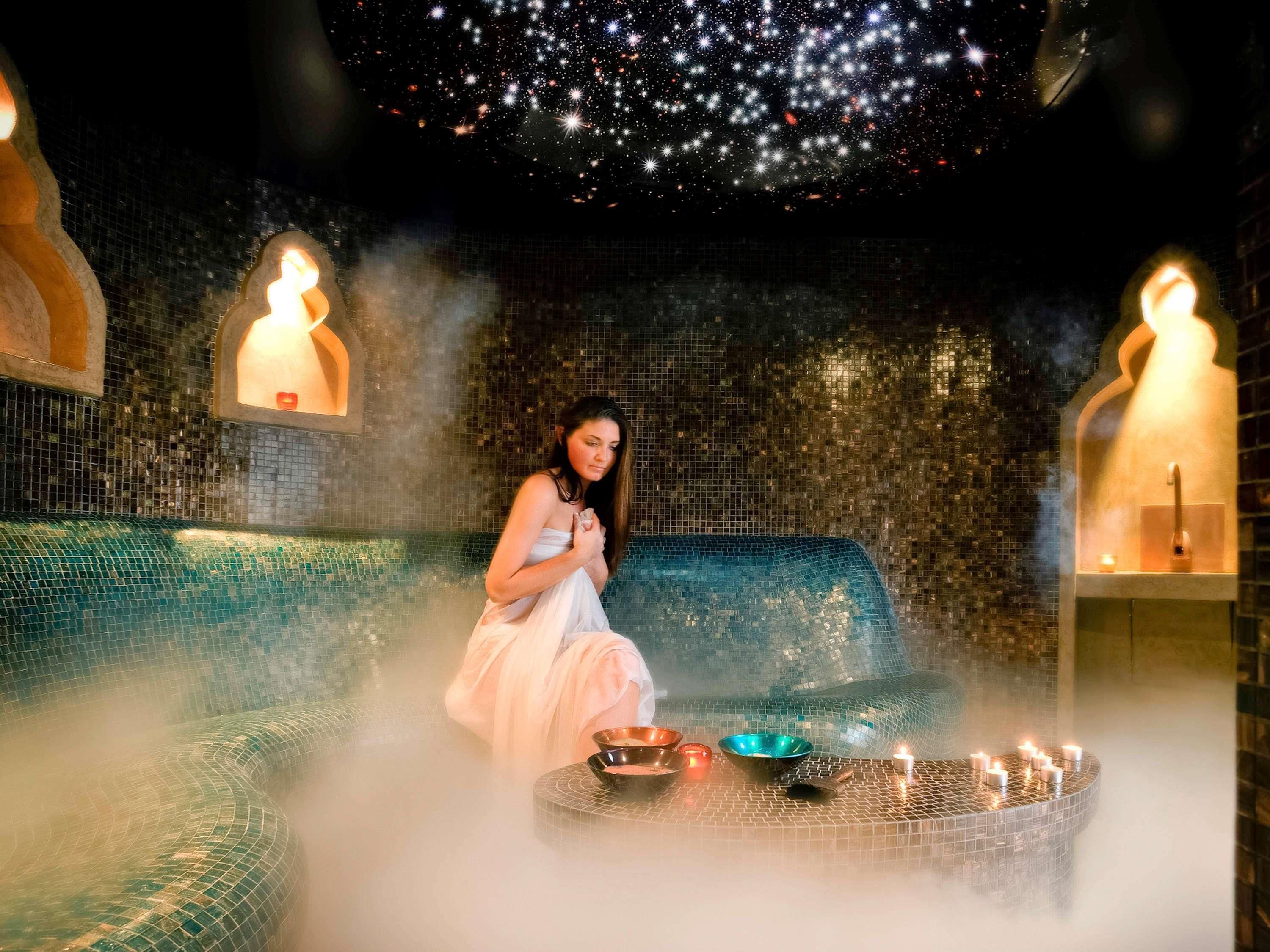 A person in a spa setting with a starry ceiling, a mosaic wall, and a steam bath.