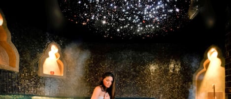 Una persona en un spa con techo estrellado, pared de mosaicos y baño de vapor.