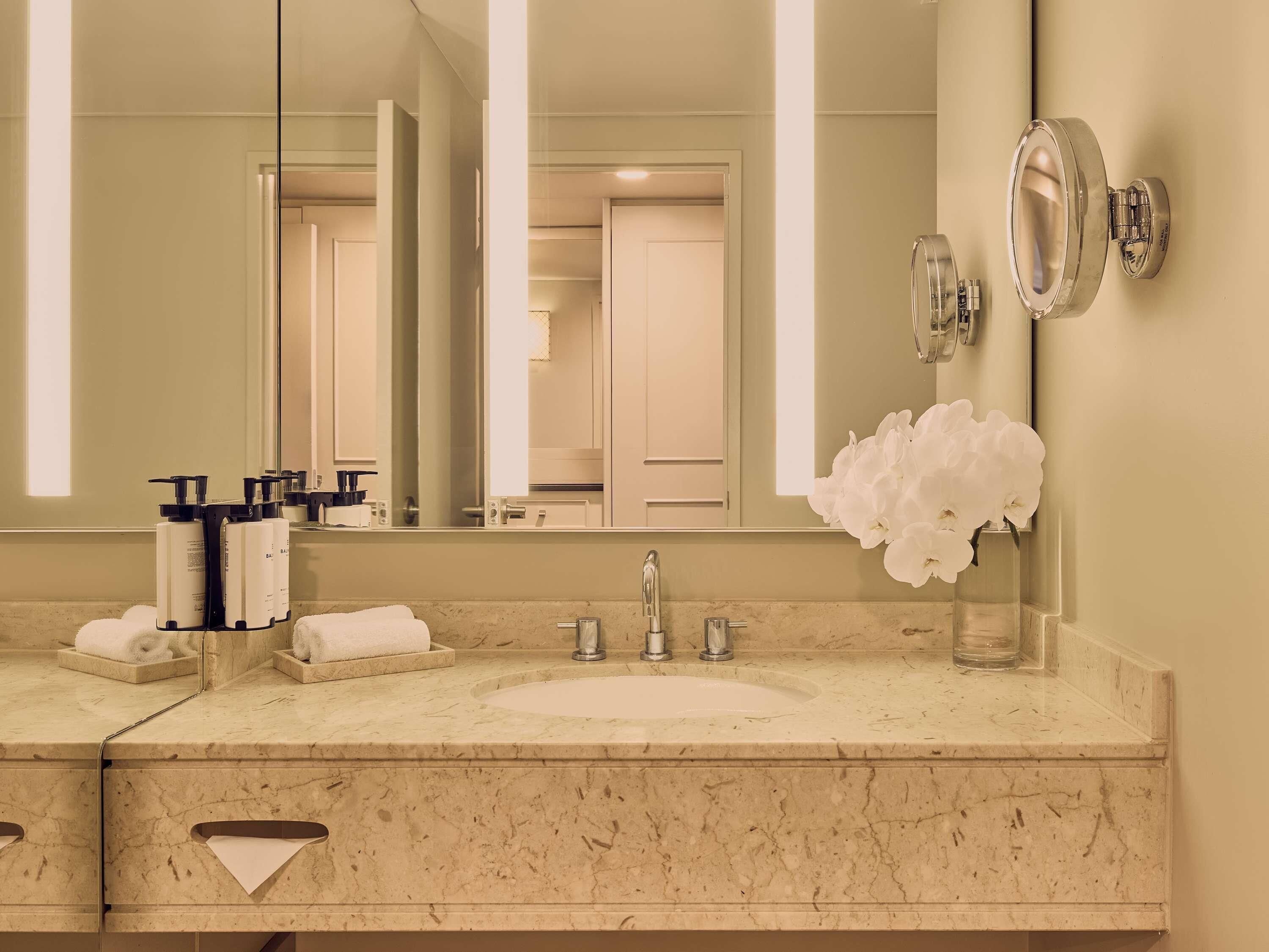 A bathroom with a marble sink, a large mirror, and a vase of white flowers.