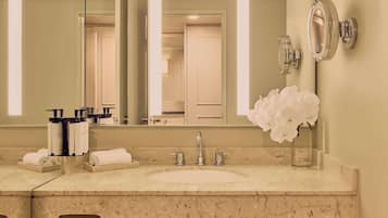 Un baño con lavamanos de mármol, un espejo grande y un florero con flores blancas.