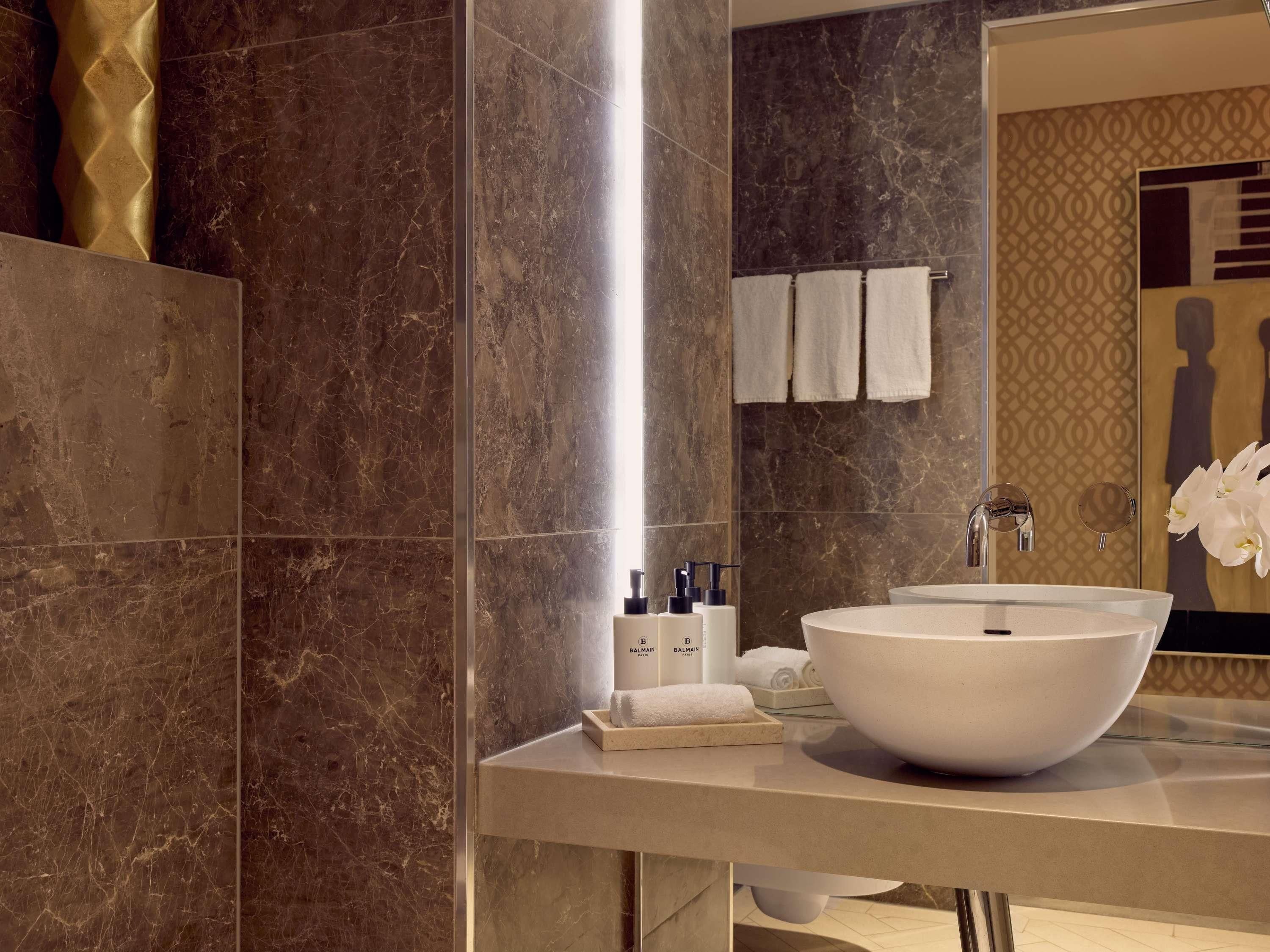 A modern bathroom with a large white vessel sink, marble walls, and a mirror with a decorative frame.