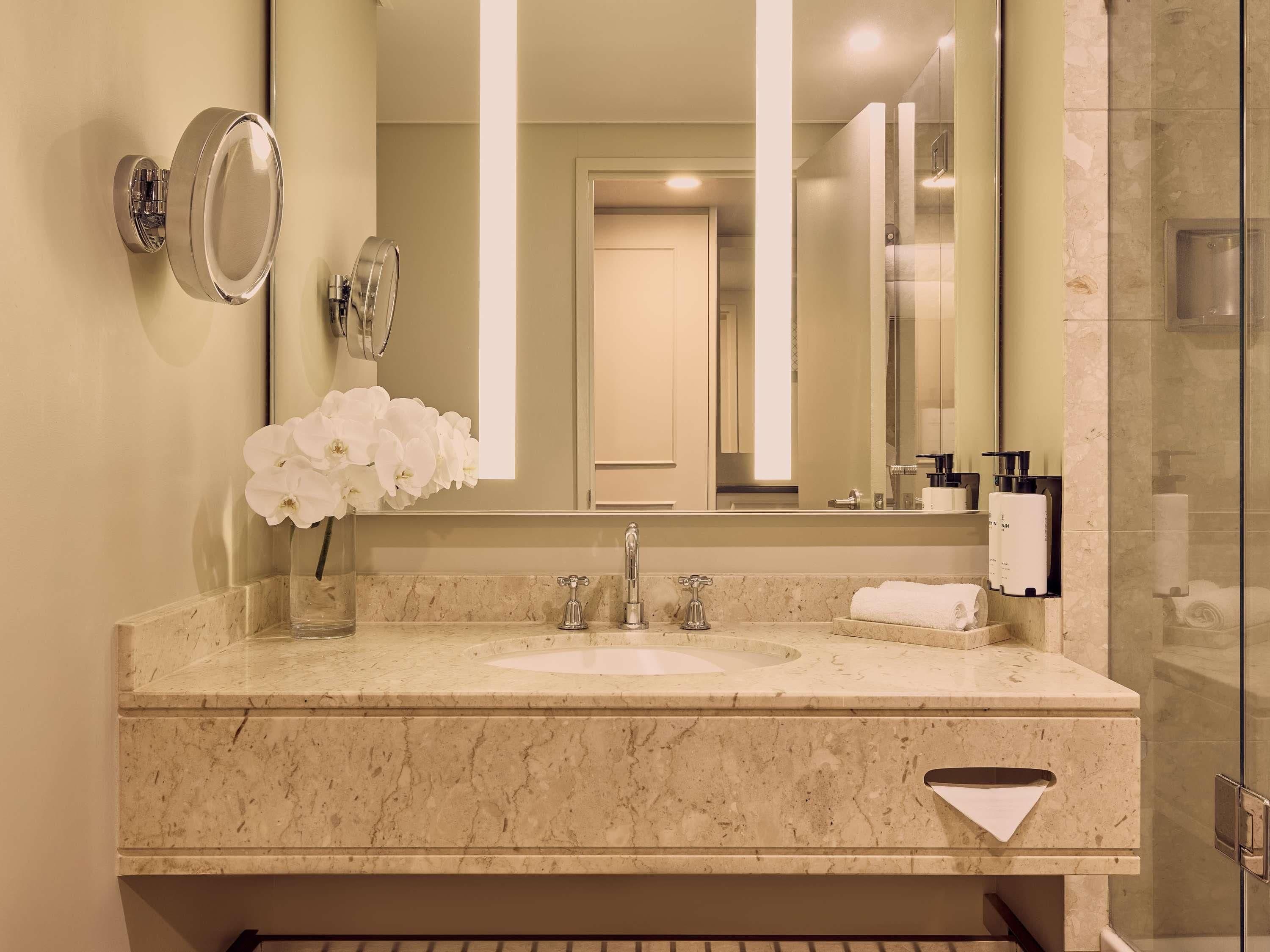 A modern bathroom with a marble sink, a large mirror, a towel rack, and a glass shower enclosure.