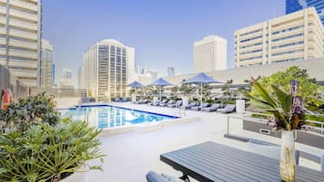 A rooftop pool area with lounge chairs, a pool, and city buildings in the background.