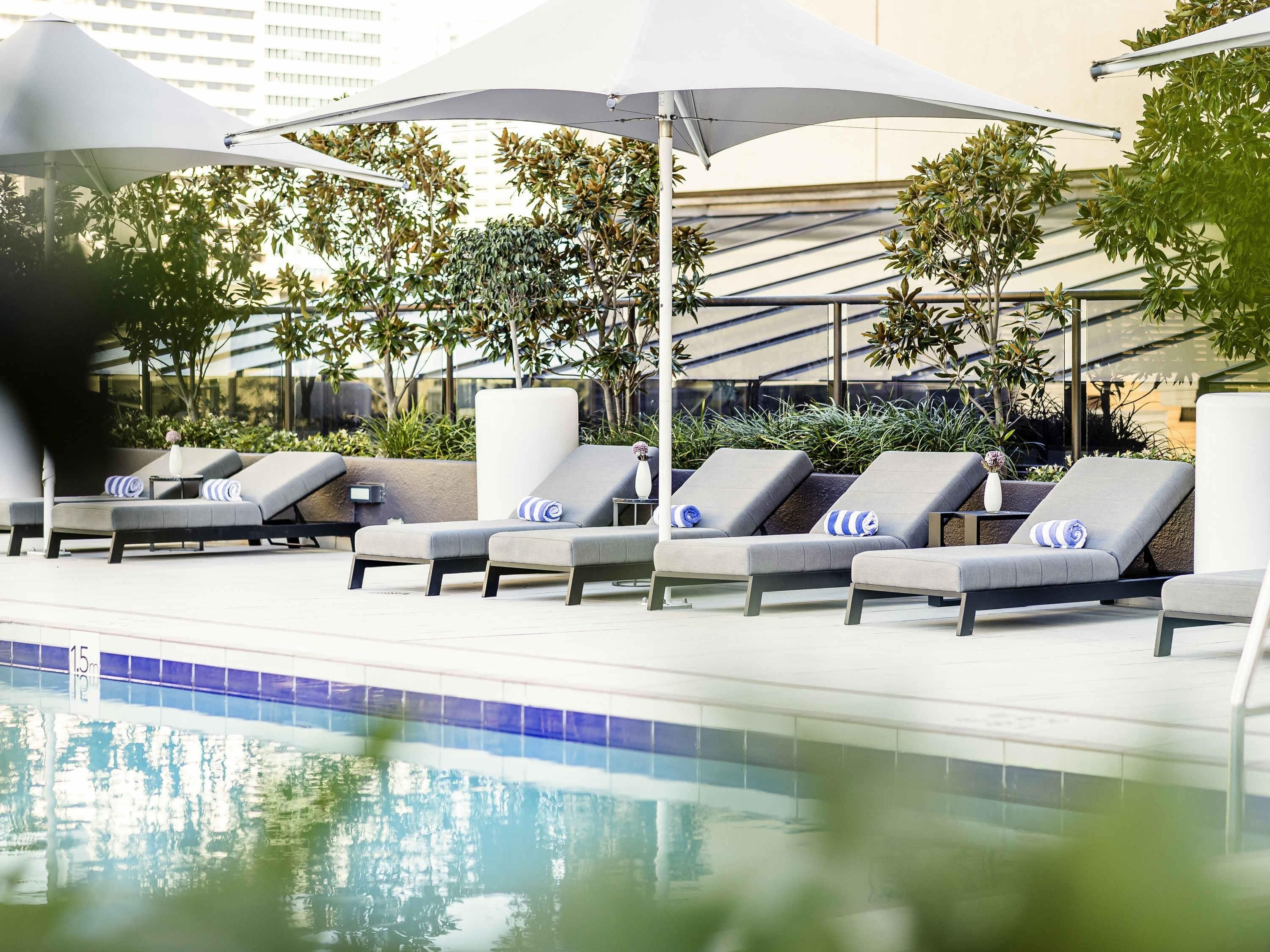 A poolside area with lounge chairs and umbrellas, surrounded by greenery and modern architecture.