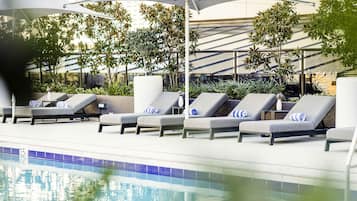 A poolside area with lounge chairs and umbrellas, surrounded by greenery and modern architecture.