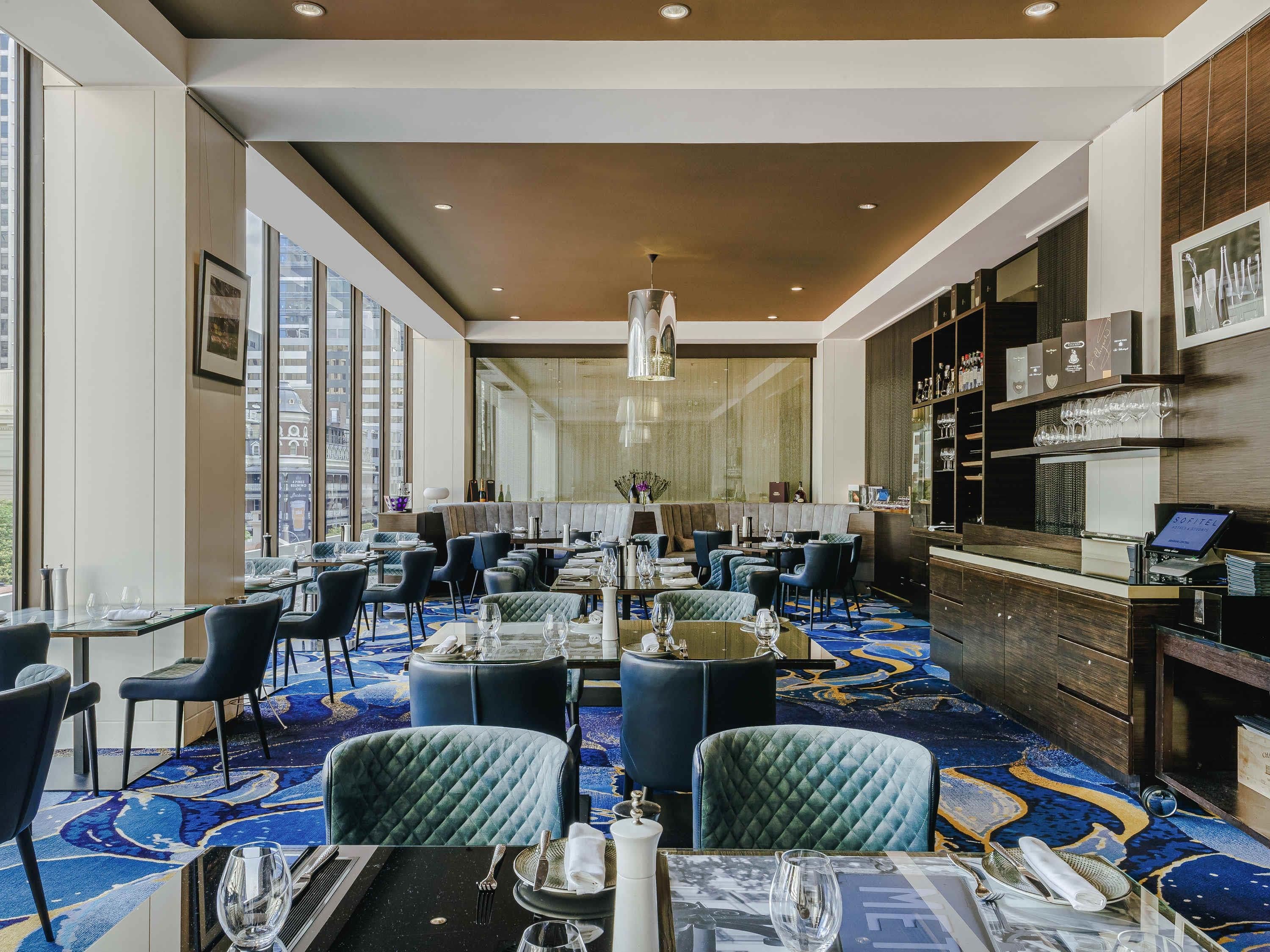 A modern restaurant with high ceilings, large windows, and a patterned carpet.